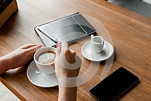 Female hands with a black phone, close-up, background of a cup of coffee, table, notebook. Business lunch