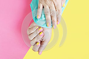 Female hands in a blue blouse with a bright pink-yellow manicure on a yellow-pink background.