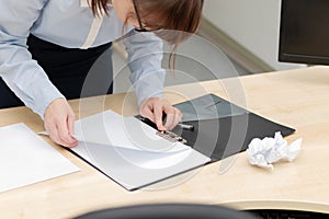 Female hands in a blue blouse in the office at a wooden work table looks through documents in a folder