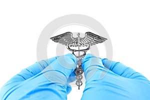 Female hands in blue disposable gloves hold a medical insignia of Caduceus isolated on white
