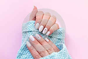 Female hands in blue knitted sweater with beautiful manicure - white ivory nails with flower on pink paper background