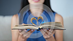 In female hands, book sheets are folded in shape of heart closeup