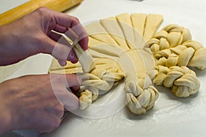 Female hands braiding, decorating dough on white kitchen table