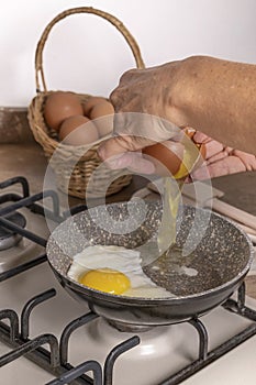 Female hands break an egg to drop it into a pan on the stove, in which another fried egg is cooking