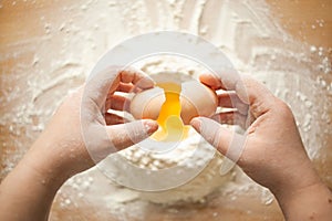 Female hands breaking a chicken egg into flour