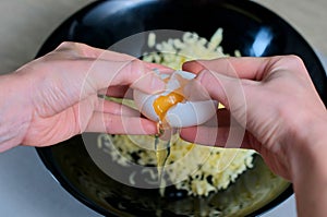 Female hands breaks a white egg into a black bowl