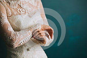 Female hands of the bride fasten buttons on the sleeve on a beautiful lace white wedding vintage dress close-up, morning preparati