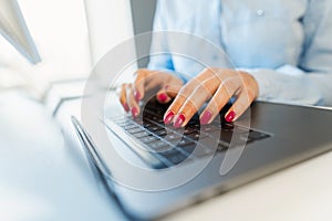 Female hands with bright manicure typing on a laptop keyboard