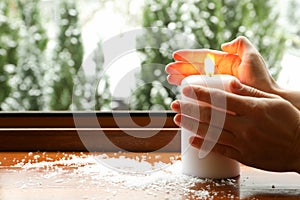 Female hands and burning candle on wooden windowsill