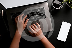 A female hands or businesswoman typing on notebook laptop keyboard on black workspace