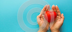 female hands carefully hold a red heart toy, blue background, . femininity, health care, checking the