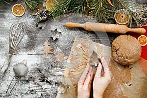 Female hands carve Christmas cookies figures in a christmas tree shape on a kitchen wooden table,  top view. Christmas mood backgr