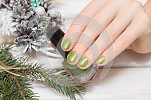 Female hands with christmas nail design. Green nail polish manicure. Woman hands hold green varnish