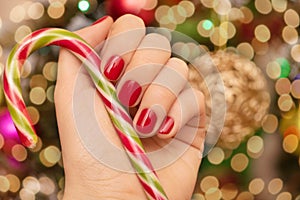 Female hands with Christmas nail design. Red nail polish manicure. Female hand hold New Year candy