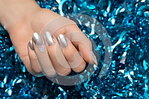 Female hands with Christmas nail design. Silver nail polish manicure. Female hand on blue New Year tinsel background