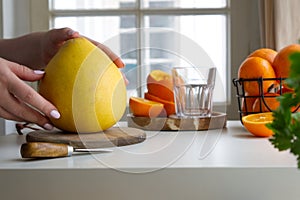 Female hands clean a pomelo standing on a wooden stand and near oranges and juice