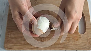 Female hands close-up clean boiled chicken egg. Home kitchen wooden table.