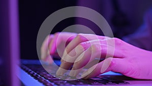 Female hands close up typing on the keyboard in neon light