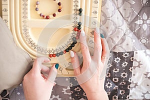 Female hands collect a bracelet from natural stones. A woman or girl and a board for collecting bracelets, necklaces.