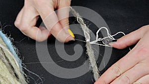 Female hands with colored nails and a needle with a thread closeup decorate artificial dreadlocks, needlework and handmade