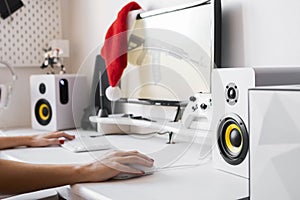 Female hands on the computer table hold a gaming mouse and keyboard. A red Santa hat hangs on the monitor.