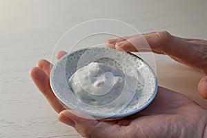 Female hands of a cosmetician holding a small bowl with mixed two component cream for a cosmetic skin treatment, copy space,