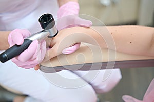 Female hands of cosmetologist examine patient hand with dermatoscope