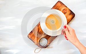 Female hands with a cup of coffee with foam over a wooden gray table, top view