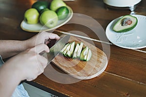 Female hands cut avocado on wooden working surface in kitchen at the home