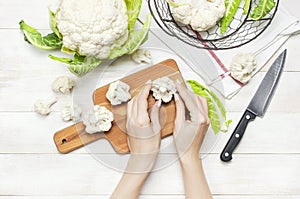 Female hands cut cauliflower with knife on cutting board, kitchen towel on rustic white wooden background top view flat lay copy