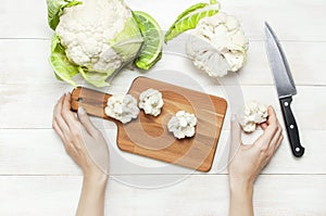 Female hands cut cauliflower with knife on cutting board, kitchen towel on rustic white wooden background top view flat lay copy