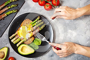 Female hands cut Grilled green asparagus wrapped with bacon, benedict poached egg and avocado on toasts for breakfast