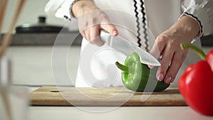 Female hands cut by knife green bell pepper on a wooden board in kitchen background