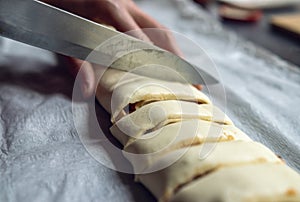 Female hands cut the rolled puff pastry into equal pieces. In the middle, there is a pepper, ham, garlic sauce, and corn.