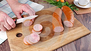 Female hands cut smoked sausage into slices on a cutting board