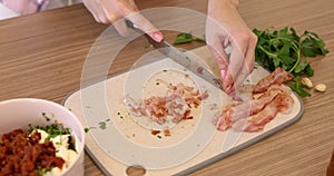 female hands cutting bacon on cutting board