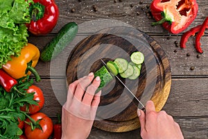 Female hands cutting cucumber at table, top view