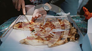 female hands cutting a delicious pizza in slices with a knife inside the box. close-up.