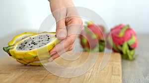 Female hands is cutting a dragon fruit or pitaya with yellow skin and white pulp with black seeds on wooden cut board on