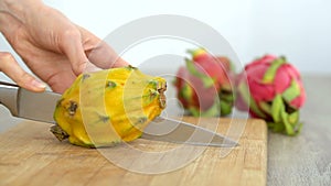 Female hands is cutting a dragon fruit or pitaya with yellow skin and white pulp with black seeds on wooden cut board on