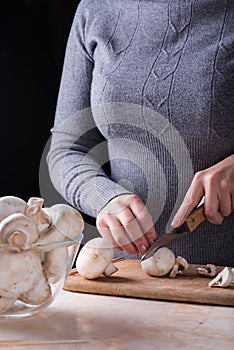 Female hands cutting fresh mushrooms on the wooden desk
