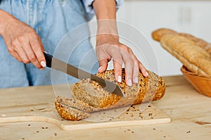 Female hands cutting grain bread on the wooden table