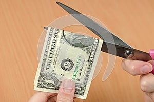 Female hands cutting one dollar bill with scissors