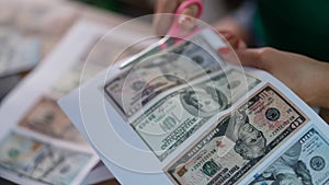 Female hands cutting out dollar bills printed on printer with scissors closeup