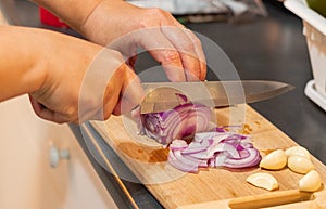 Female hands cutting red onion and garlic on the wooden board. Close up  selective focus