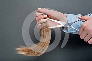 Female hands demonstrate scissors and cut hair on a dark background
