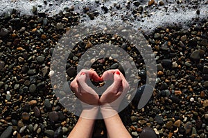 female hands depict a heart on the background of wet pebbles