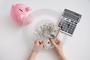 Female hands with dollars, piggy bank and calculator on white background, top view