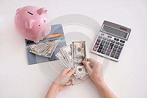 Female hands with dollars, piggy bank, wallet and calculator on white background, top view