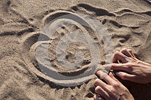 Female hands draw heart on dry sand on the beach on a sunny day.